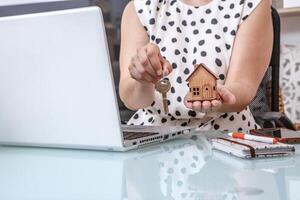 Real Estate Agent Holding Wooden House Model and Keys at Home Office Desk photo