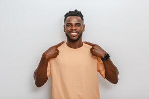 Smiling man wearing a casual peach shirt points at himself against a neutral background in a studio setting photo