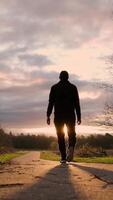 a man walking down a path with the sun setting infront of him video