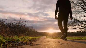 a man walking down a path with the sun setting infront of him video