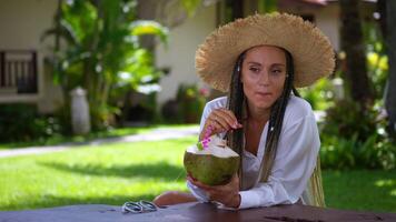 Happy smiling woman tourist in straw hat with fresh green coconut in hands enjoying summer weekend. A light wind shakes her hat. Summer weekend concert video