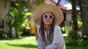 Portrait glad woman tourist enjoying summer cold drink banana fresh juice, resting on summer vacation. Woman in sunglasses and hat drinking orange juice at summertime. Concept resting on vacation video