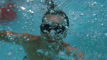 Funny man in sunglasses enjoys summer days, sunbathing swims in the pool and dives underwater filming himself with an action camera making a selfie . POV . video