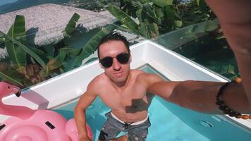 Selfie man filming himself on action camera as he jumps in pool during summer vacation. Active man on glasses jumps in the pool and filming himself as he dives underwater during summer vacation video