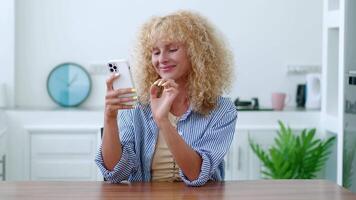 Charming Caucasian redhead young woman, in casual wear, relaxing at home, using mobile phone, typing text on her smartphone, browsing websites, surfing the internet, networking. Online communication video
