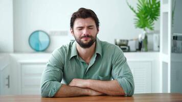 Frustrated young man sitting at the kitchen table in the home interior, experiencing panic attacks and stress, looking around trying to find a solution to problem and get out of a hopeless situation video