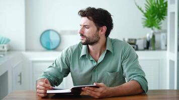 Handsome dark-haired young Caucasian man relaxing at home, leafing through the pages while reading interesting hardcover book, thoughtfully looking aside. Erudition. Litterature. Education. Knowledge video
