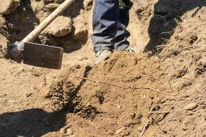 legs of a man moving soil with a hoe at a work site, archeologist working concept photo