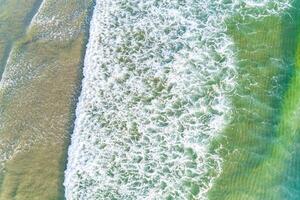 Aerial top view of beautiful sand beach with wave foam and turquoise sea, directly above view from drone. Summer concept background photo