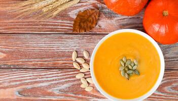Autumn composition with pumpkin cream soup and pumpkins on a wooden table. Copy space. Top view. photo