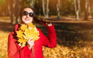 Smiling young girl with yellow leaves enjoys a warm autumn day in the park. Hello, Autumn. Selective focus. photo