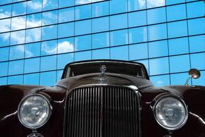 Vintage, black, shiny car on a background of a mirrored wall of a modern building. photo
