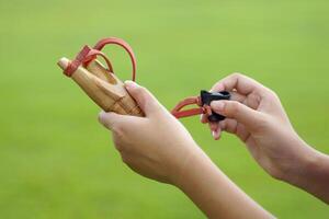 Hand holding Slingshot on green background It is a weapon made from a forked stick with rubber attached to a leather strip that holds bullets to be fired. photo