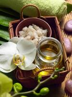 A tranquil spa setting featuring an orchid, essential oils, and rough sugar crystals, set against a backdrop of vibrant green leaves and a soft towel. photo