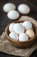 A rustic bowl filled with white and brown eggs on a textured burlap surface photo