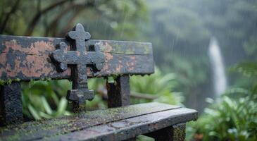 Rainy Outdoor Bench With Cross Symbol Near Waterfall Surrounded By Lush Greenery photo