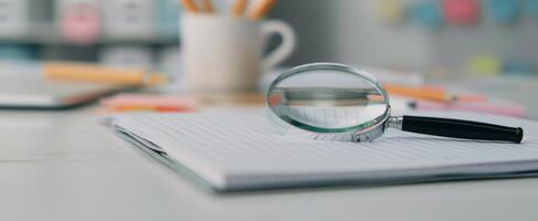 Magnifying Glass on Blank Notebook Surrounded by Neutral Background photo