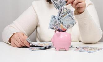 Pink ceramic piggy bank and woman with American paper money. Wealth concept, bargain, accumulation. High profitable margin photo