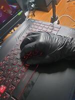 Black gloved hands rest on the red-lit keyboard of a computer notebook. photo