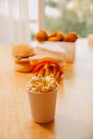 A bucket of popcorn, top-view, warm colors, light brown wooden background, flat lay, daylight macro close-up photo