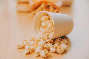 A bucket of popcorn, top-view, warm colors, light brown wooden background, flat lay, daylight macro close-up photo