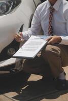 Side view of writing on clipboard while insurance agent examining car after accident photo