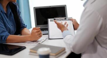 Doctor and patient sitting near each other at the wooden desk in clinic. Female physician's pointing to a records form. Medicine concept photo