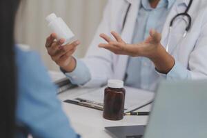 Doctor and patient sitting near each other at the wooden desk in clinic. Female physician's pointing to a records form. Medicine concept photo