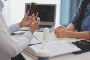 Doctor and patient sitting near each other at the wooden desk in clinic. Female physician's pointing to a records form. Medicine concept photo