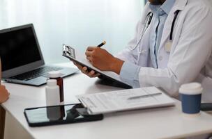 Doctor and patient sitting near each other at the wooden desk in clinic. Female physician's pointing to a records form. Medicine concept photo