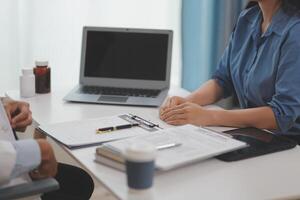 Doctor and patient sitting near each other at the wooden desk in clinic. Female physician's pointing to a records form. Medicine concept photo