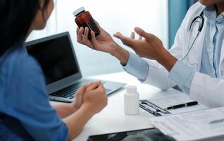 Doctor and patient sitting near each other at the wooden desk in clinic. Female physician's pointing to a records form. Medicine concept photo
