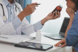 Doctor and patient sitting near each other at the wooden desk in clinic. Female physician's pointing to a records form. Medicine concept photo