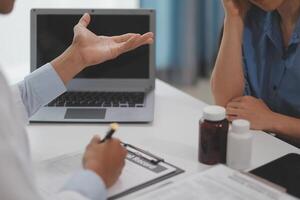 Doctor and patient sitting near each other at the wooden desk in clinic. Female physician's pointing to a records form. Medicine concept photo