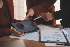 Group of confident business people point to graphs and charts to analyze market data, balance sheet, account, net profit to plan new sales strategies to increase production capacity. photo