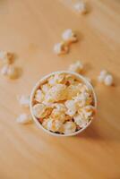 A bucket of popcorn, top-view, warm colors, light brown wooden background, flat lay, daylight macro close-up photo