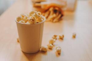 A bucket of popcorn, top-view, warm colors, light brown wooden background, flat lay, daylight macro close-up photo