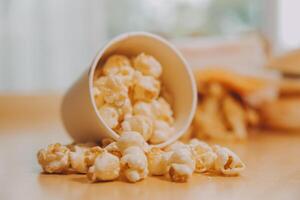 A bucket of popcorn, top-view, warm colors, light brown wooden background, flat lay, daylight macro close-up photo