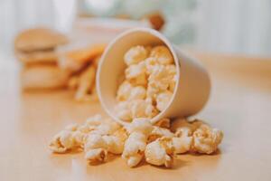 A bucket of popcorn, top-view, warm colors, light brown wooden background, flat lay, daylight macro close-up photo