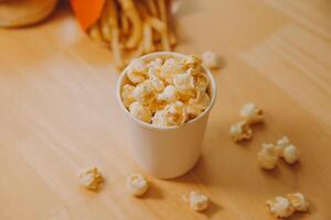 A bucket of popcorn, top-view, warm colors, light brown wooden background, flat lay, daylight macro close-up photo