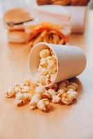 A bucket of popcorn, top-view, warm colors, light brown wooden background, flat lay, daylight macro close-up photo
