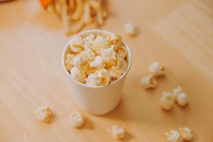 A bucket of popcorn, top-view, warm colors, light brown wooden background, flat lay, daylight macro close-up photo