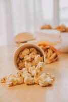 A bucket of popcorn, top-view, warm colors, light brown wooden background, flat lay, daylight macro close-up photo