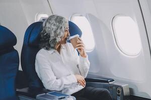 An attractive, elegant Asian businesswoman is sipping coffee while looking at the view outside the plane window, traveling on a business trip. businesspeople, transportation, luxurious lifestyle photo