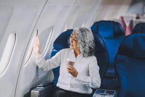 An attractive, elegant Asian businesswoman is sipping coffee while looking at the view outside the plane window, traveling on a business trip. businesspeople, transportation, luxurious lifestyle photo