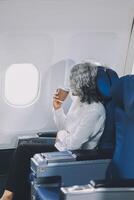 An attractive, elegant Asian businesswoman is sipping coffee while looking at the view outside the plane window, traveling on a business trip. businesspeople, transportation, luxurious lifestyle photo