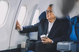 Attractive Asian male passenger of airplane sitting in comfortable seat while working laptop and tablet with mock up area using wireless connection. Travel in style, work with grace. photo