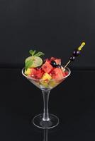 A glass with fruit and a spoon on a black background photo