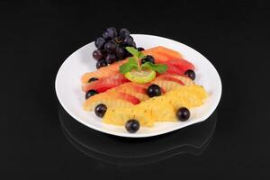 A plate of fruit with grapes, oranges, and lemons photo