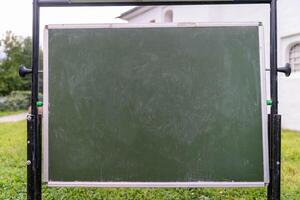 A chalkboard is positioned on grass, covered in scribbles and marks photo